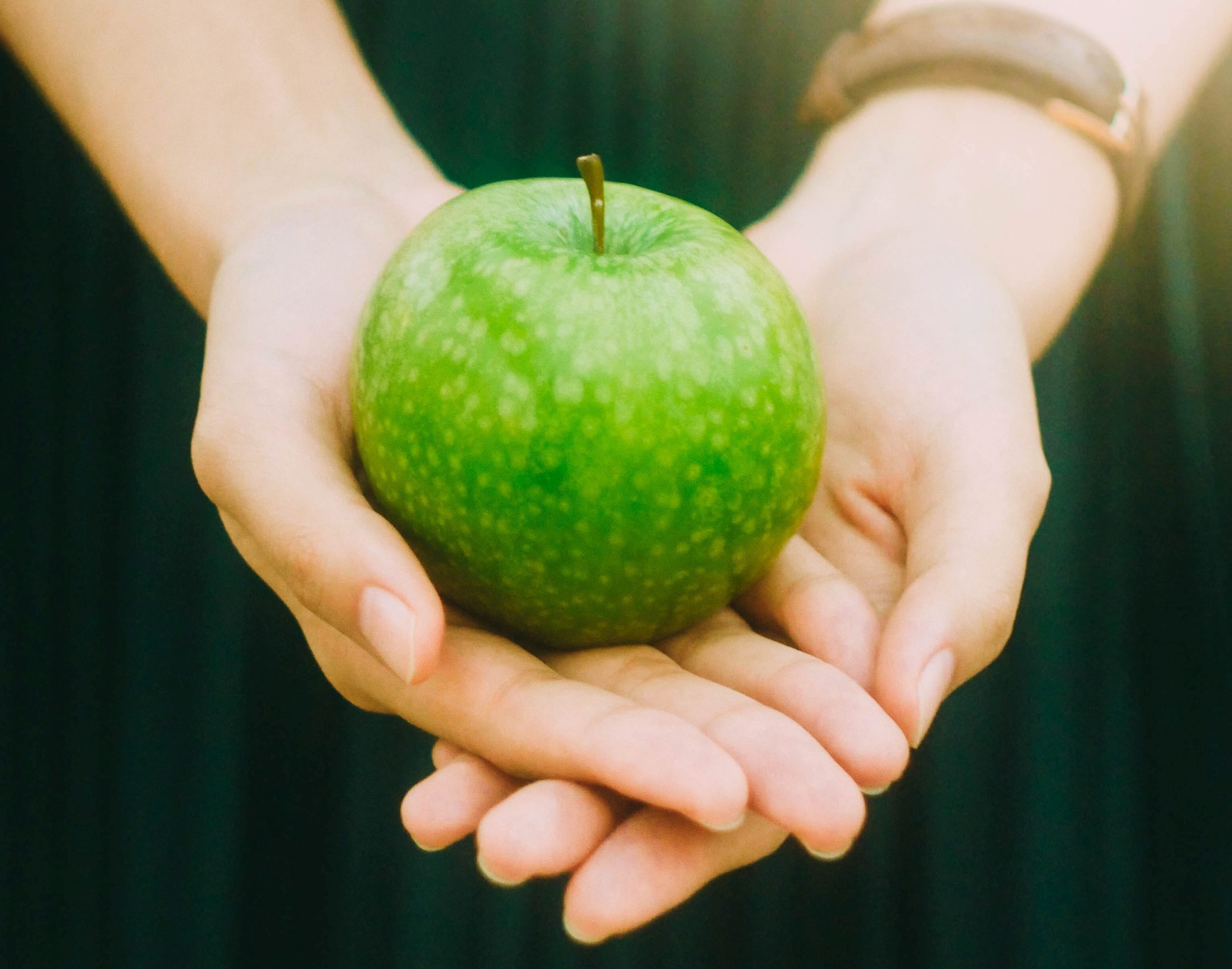 two hands holding a green apple